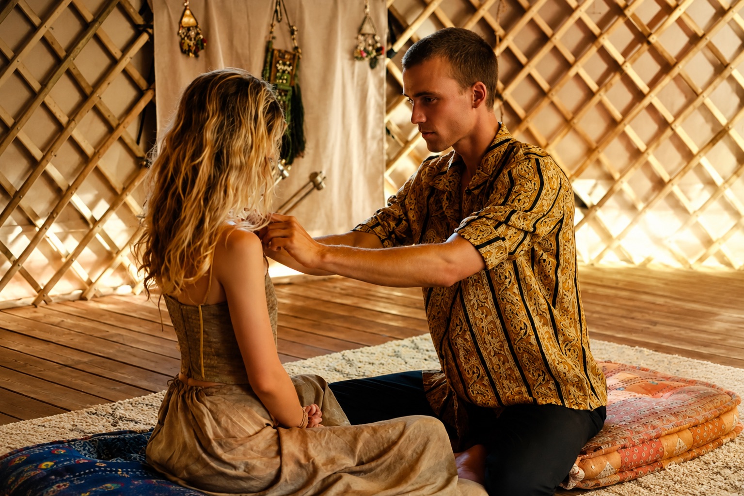 Marc Lüloh adjusting a ceremonial garment by candlelight inside a woven tent, preparing a private journey.
